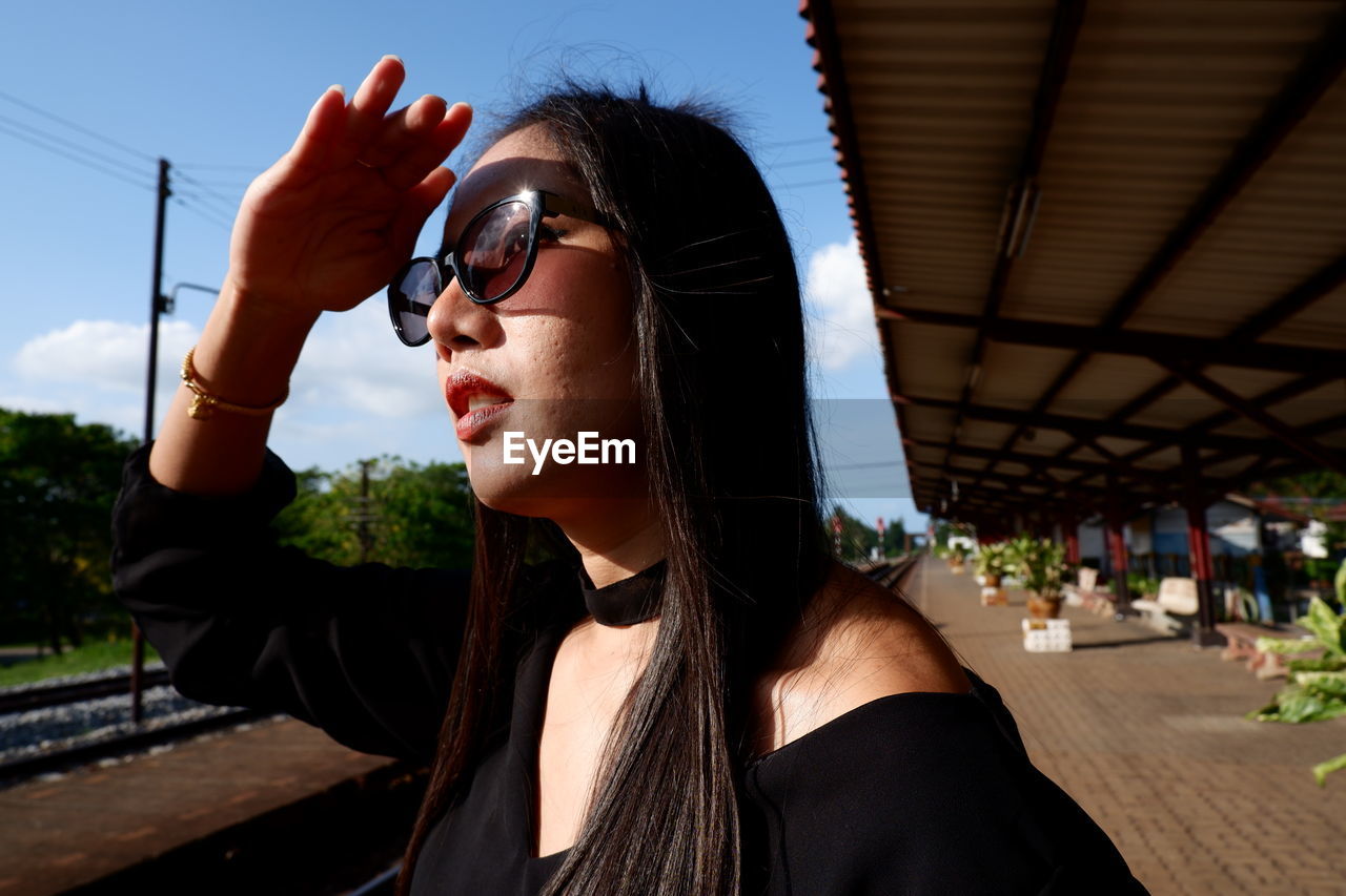 Close-up of woman shielding eyes while standing at railroad station platform