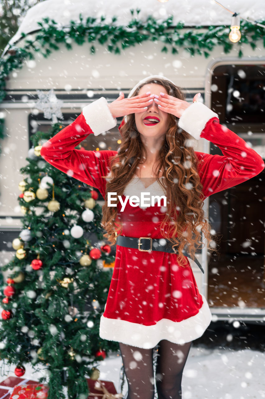 portrait of young woman with umbrella standing against christmas tree