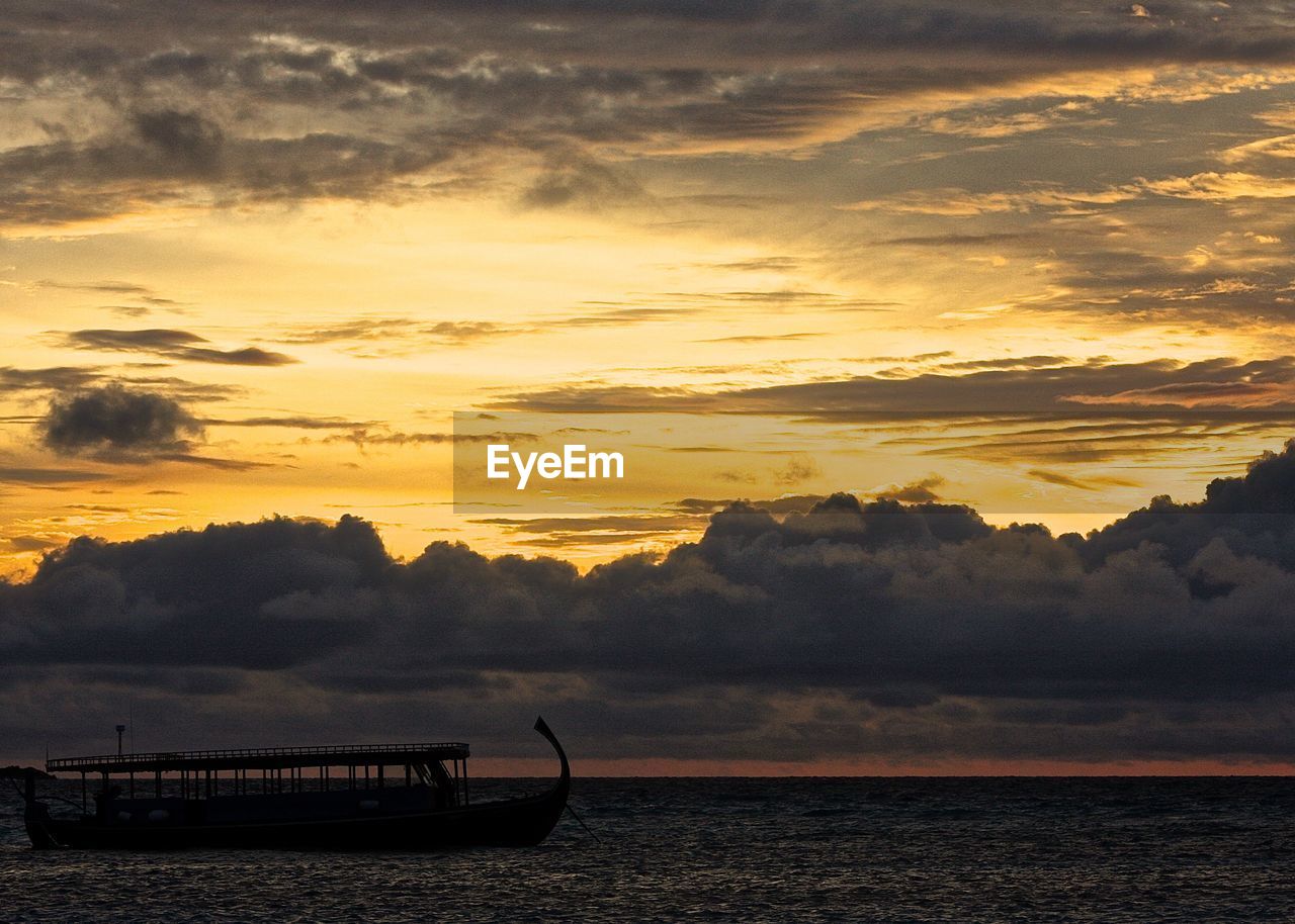 Boat sailing in sea against cloudy orange sky during sunset