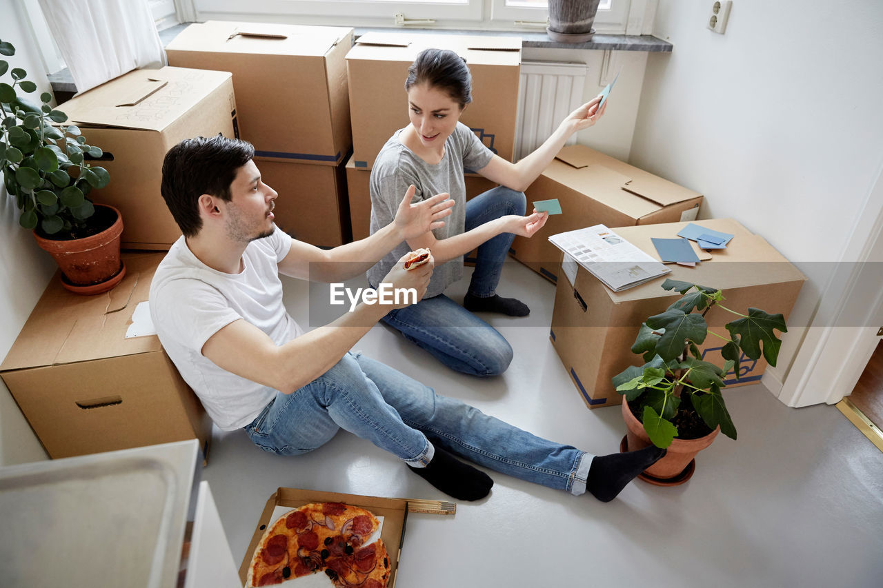 Couple discussing over color swatches while having pizza at new home