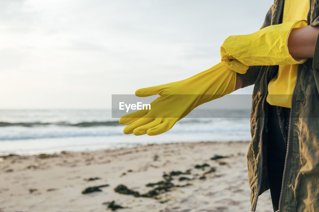 Woman standing and wearing protective glove for cleaning beach against sky
