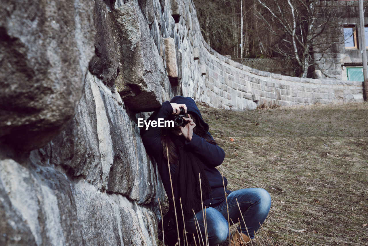 Woman photographing while crouching by retaining wall