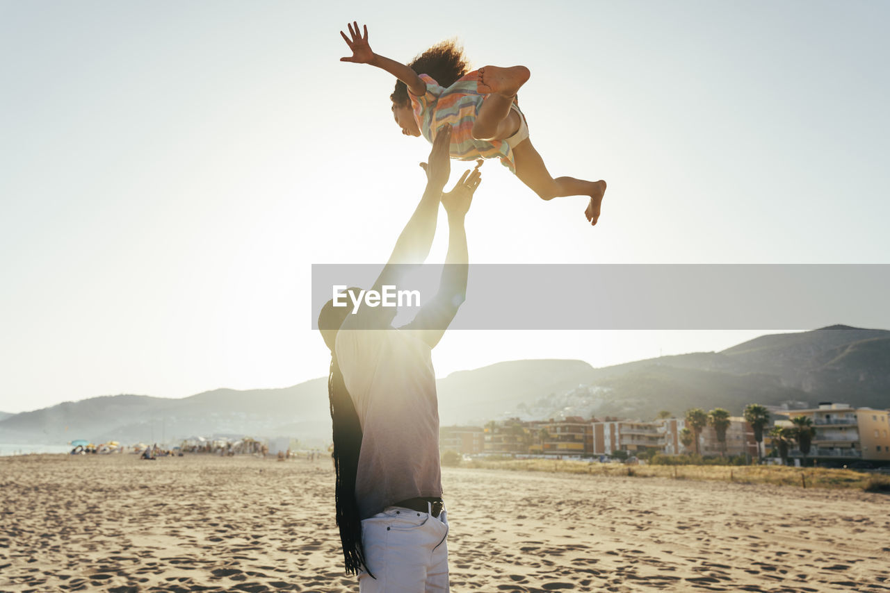 Playful father throwing daughter in air at beach