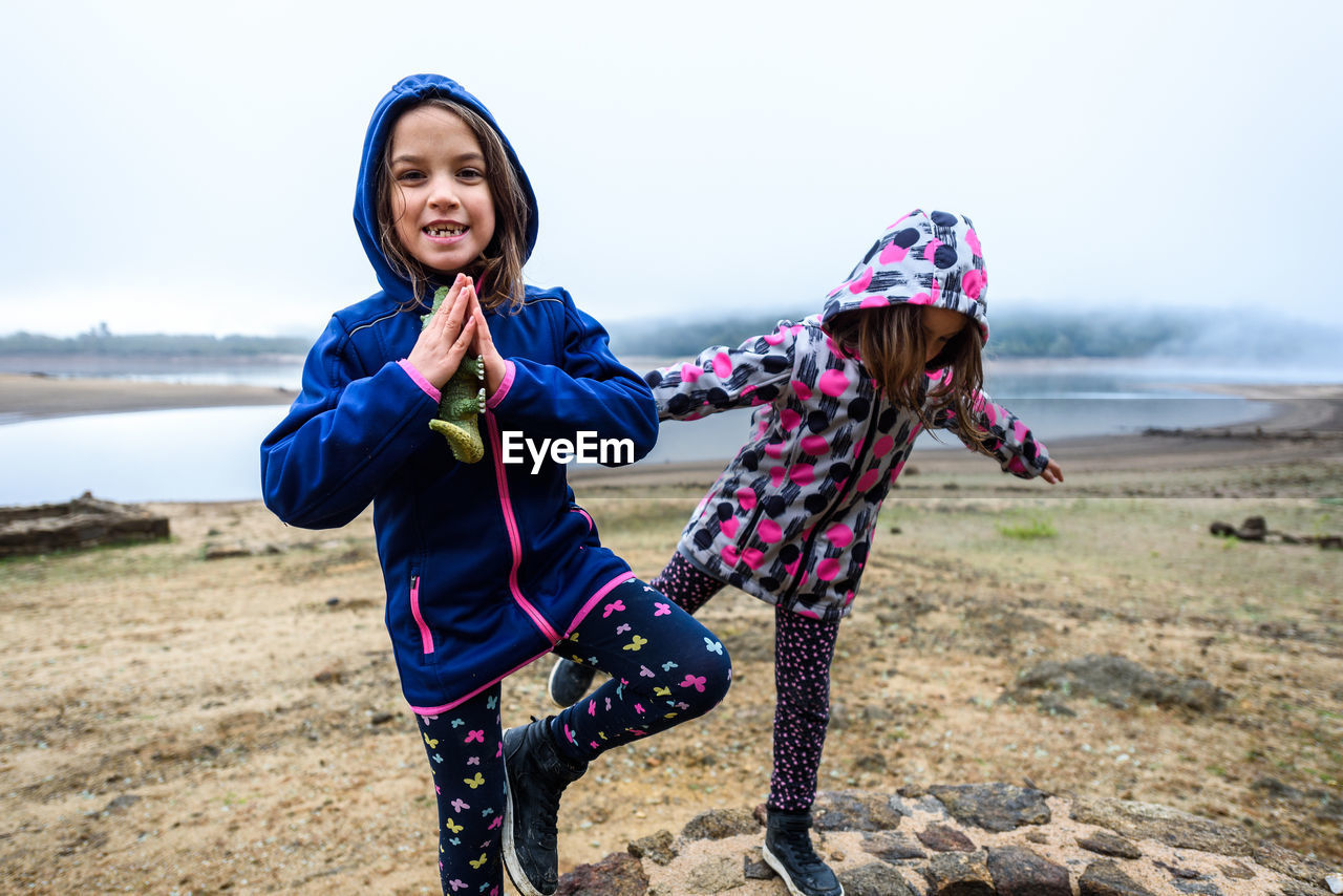 Sisters standing on water well against sky