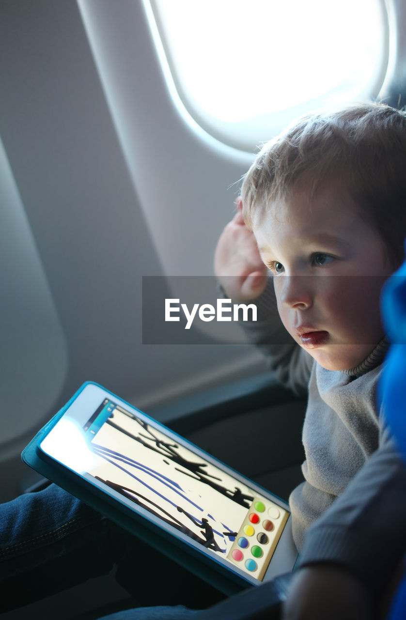 Close-up of boy with digital tablet in airplane