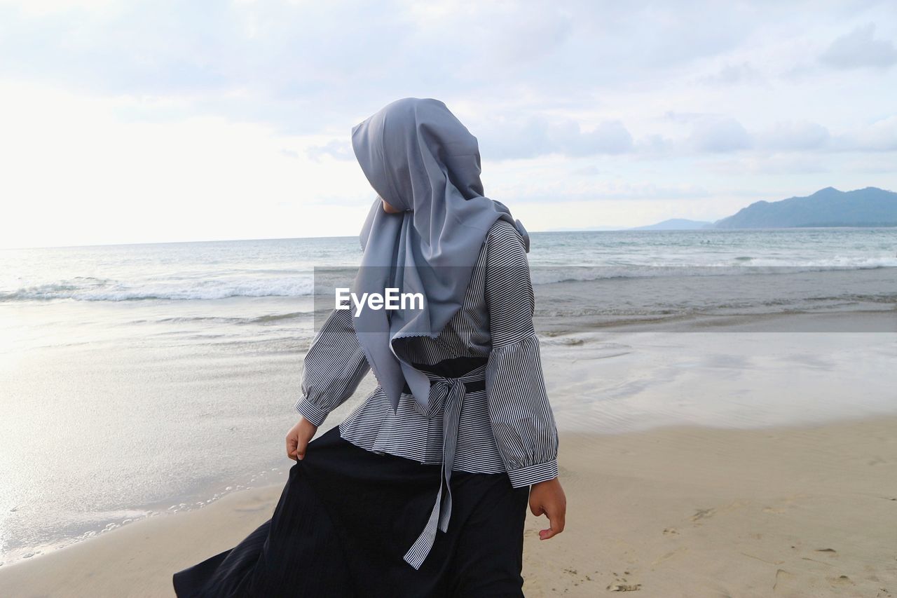 A muslim girl is looking backwards with the background of the sea
