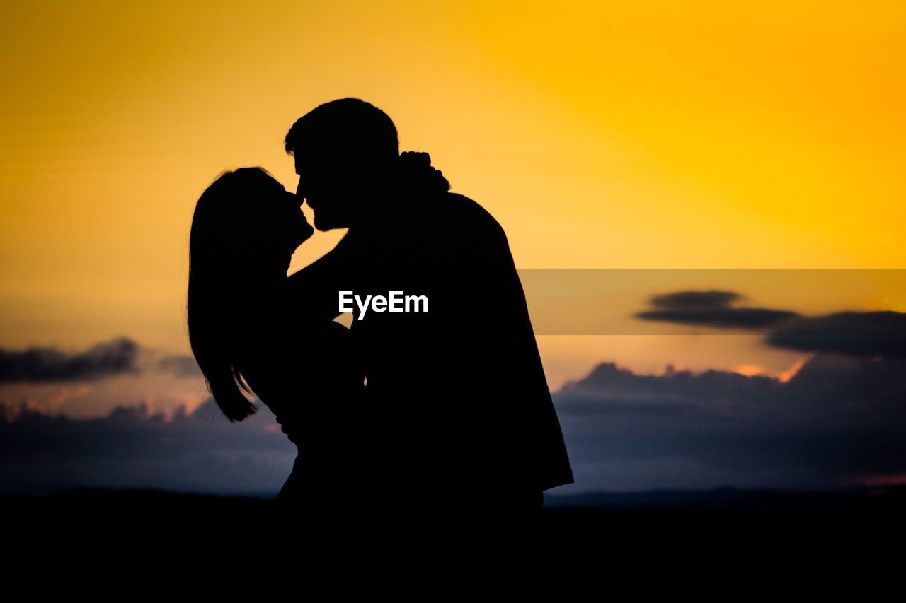 Silhouette couple hugging against sky during sunset