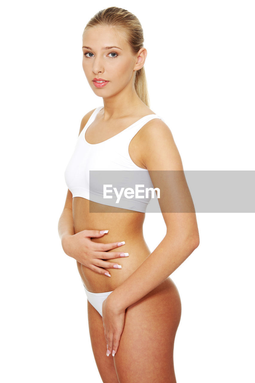 Portrait of a beautiful young woman touching abdomen against white background