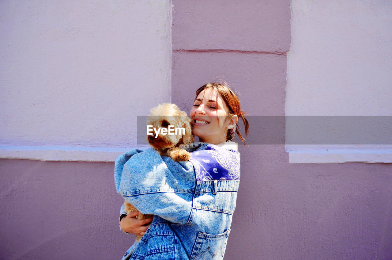 Happy woman with dog standing against wall