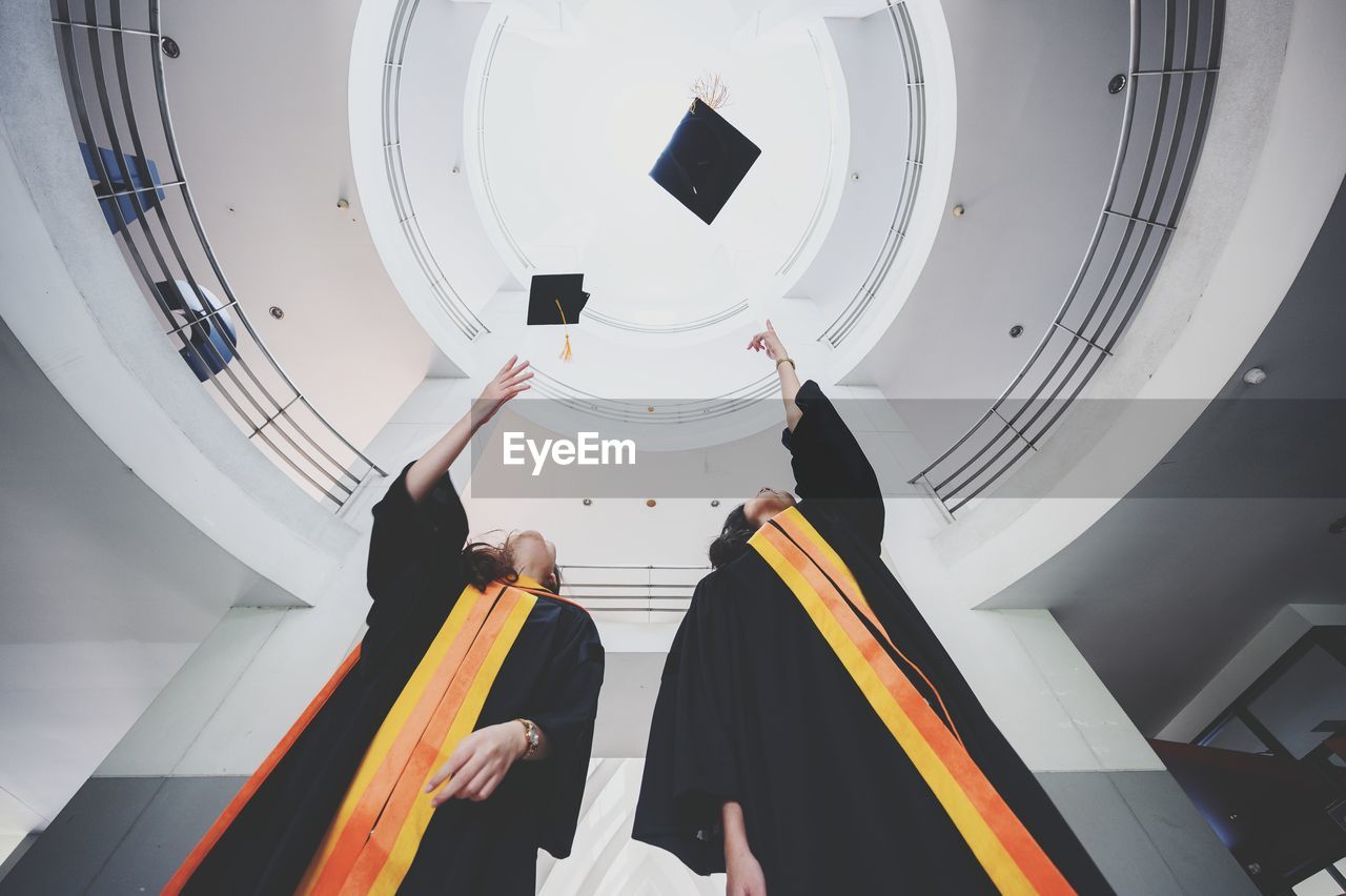 Low angle view of women in graduation gowns while standing in building