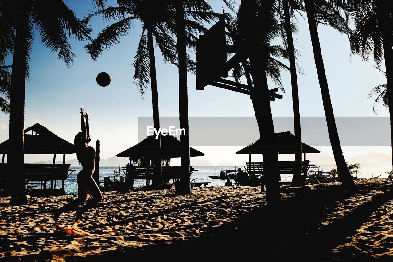 Woman playing volleyball at beach against trees