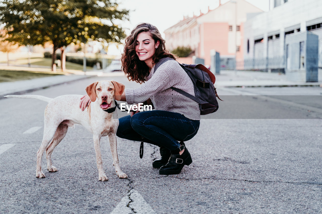 Smiling woman with dog on road in city