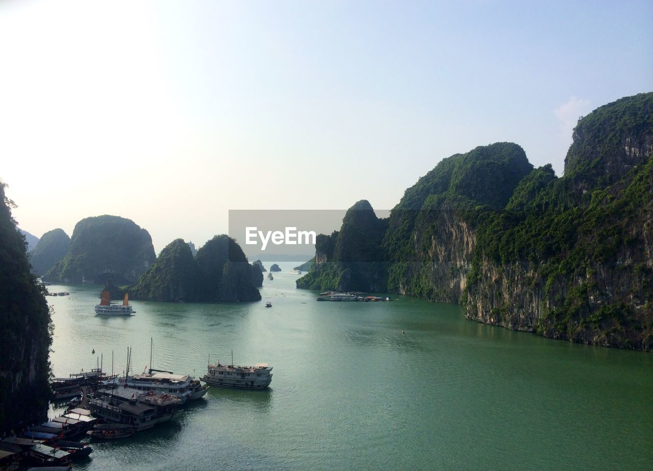 Ferries on sea by rocks against clear sky at halong bay