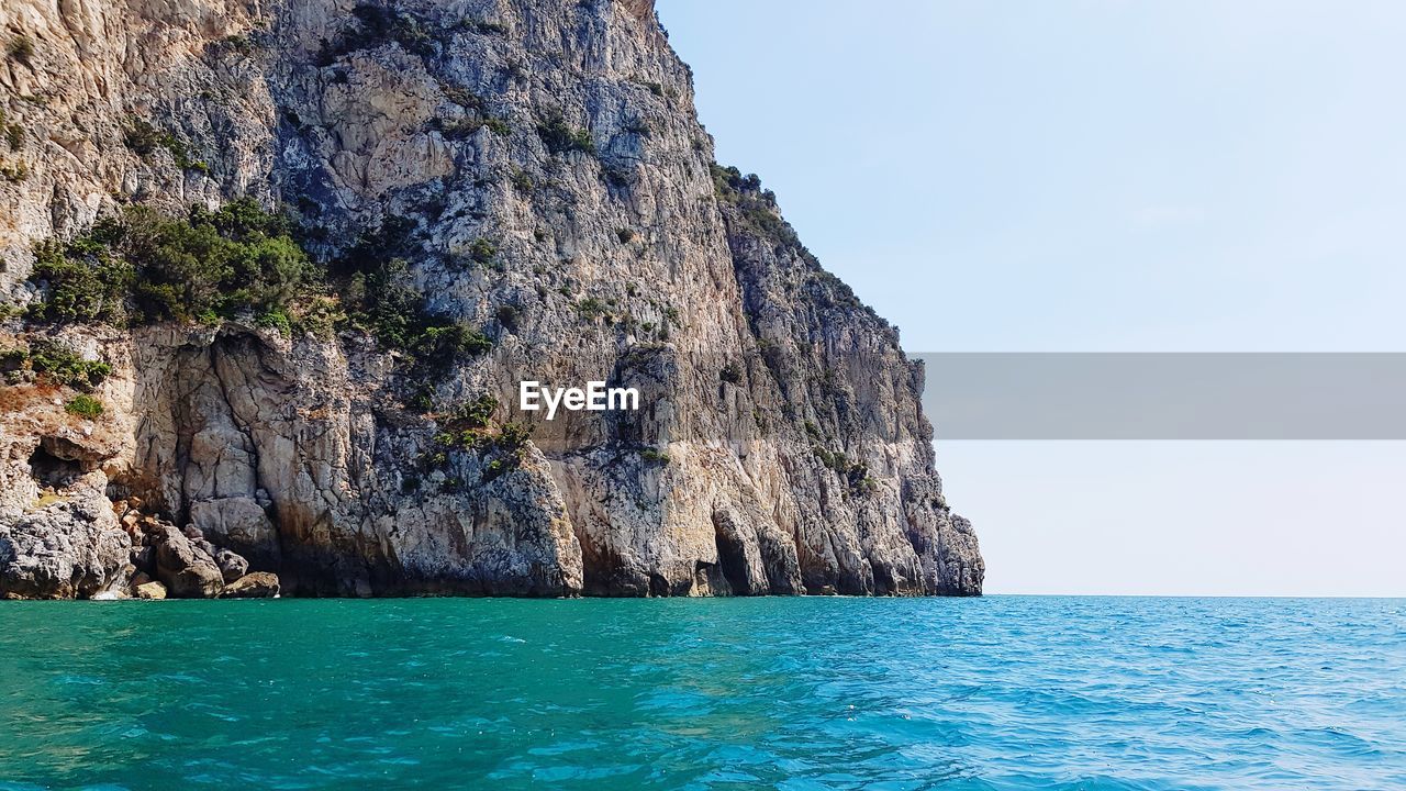 Rock formations by sea against clear sky