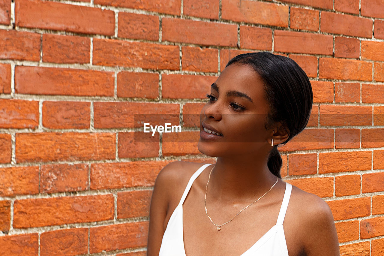 Close-up of woman looking away while standing against brick wall