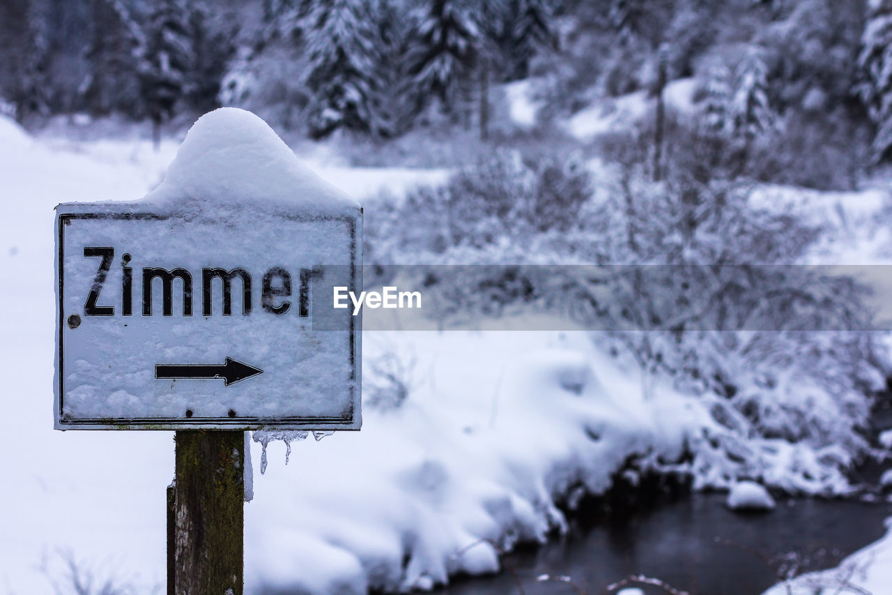 Snow covered information sign by stream against field