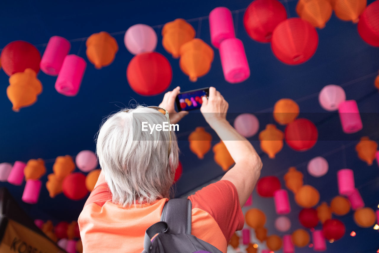 Rear view of woman photographing lanterns in sky