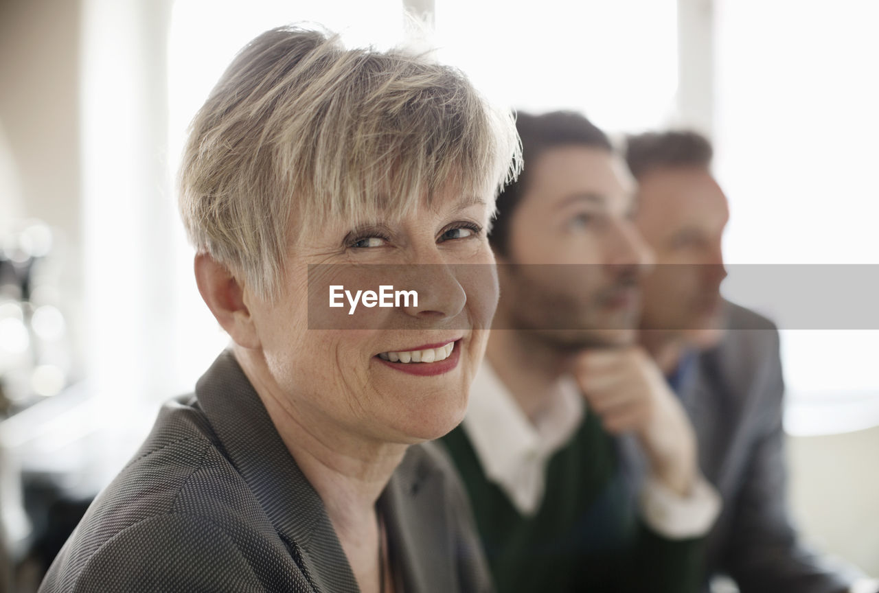 Portrait of happy businesswoman with colleagues in background at office