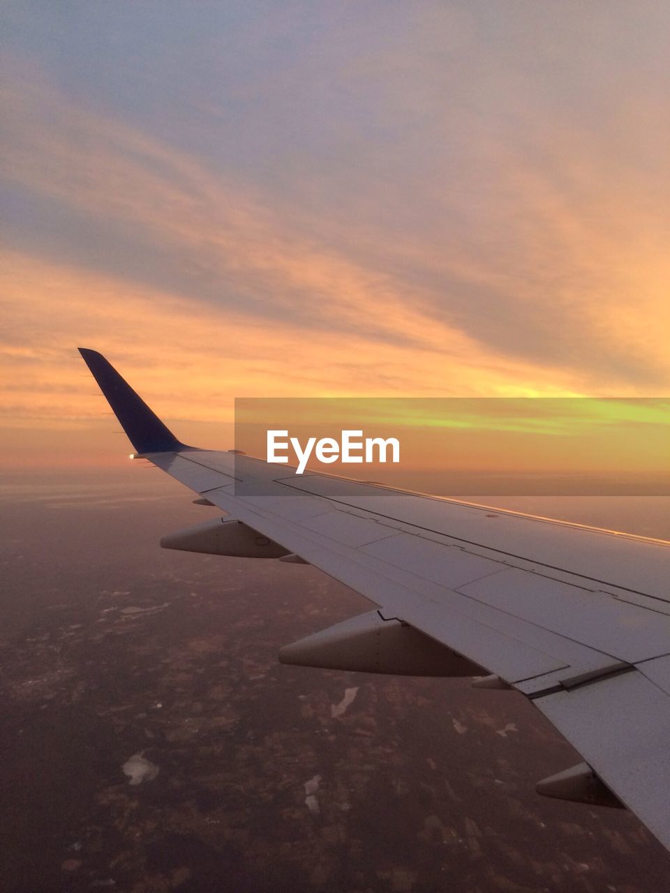 Cropped image of airplane flying over landscape against sky at sunset