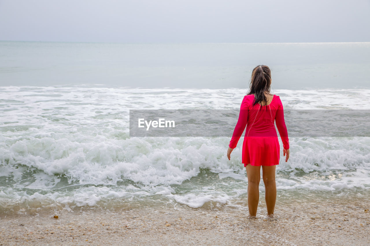 Rear view of girl standing in sea against sky