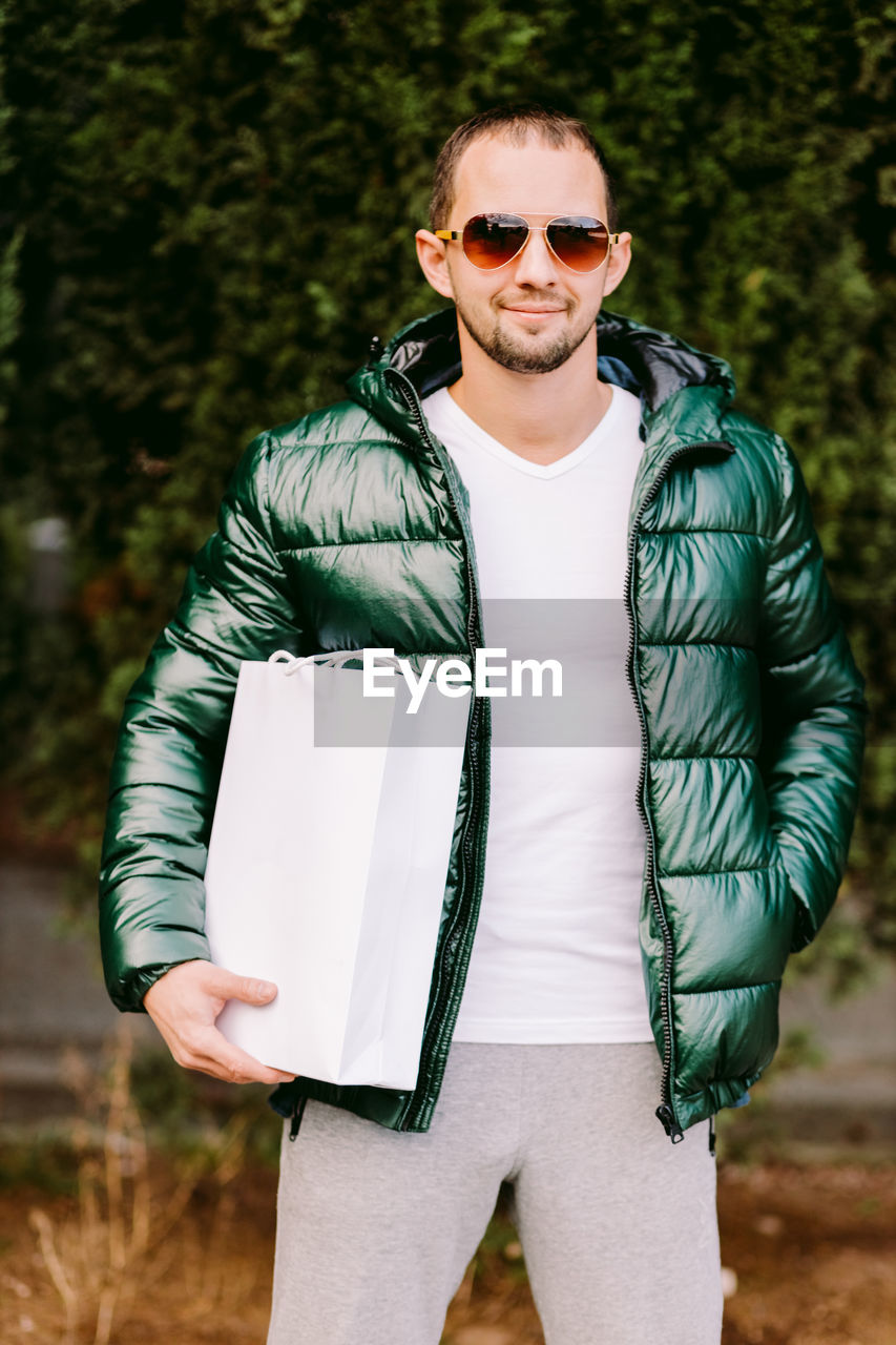 Portrait of young man wearing sunglasses holding shopping bag