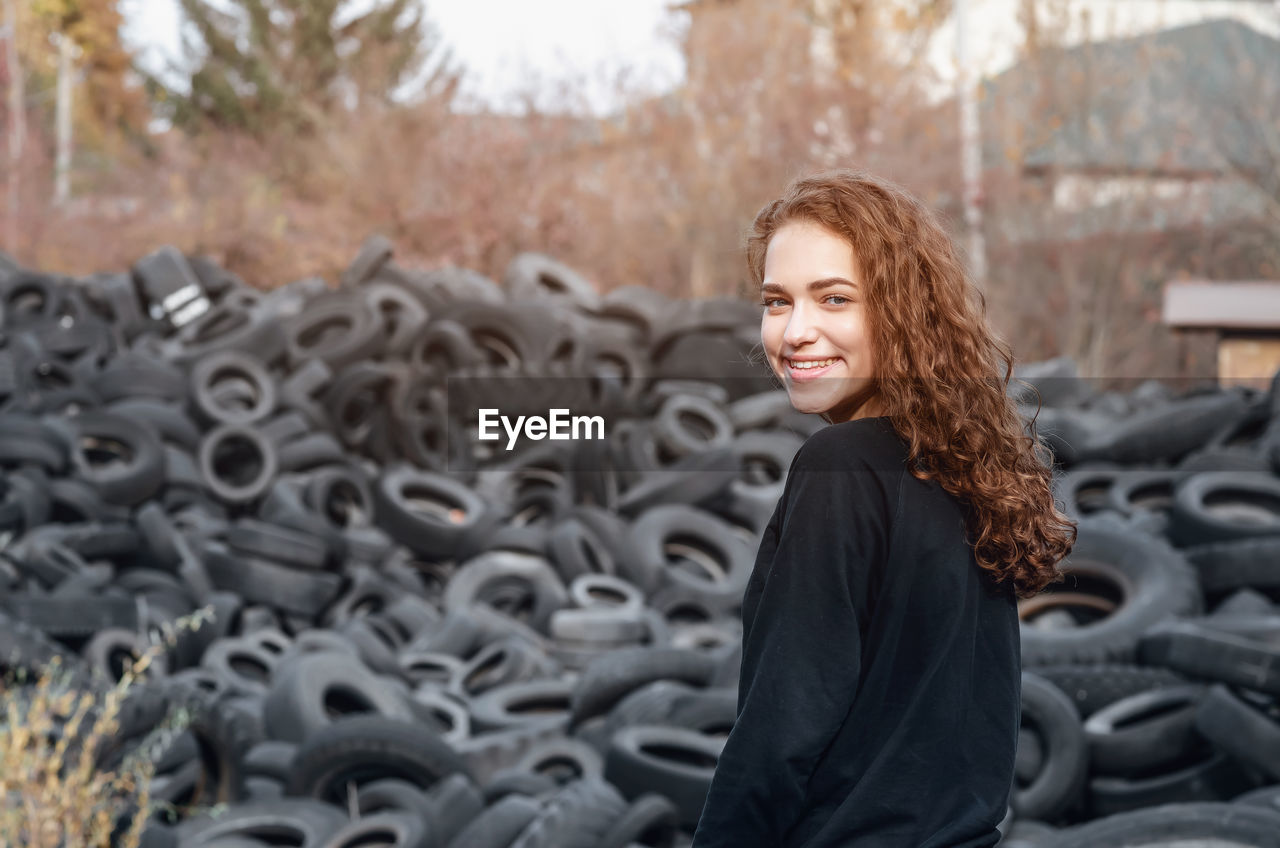 Curly girl with beaming smile on the background of pile of tires. ecological problems.