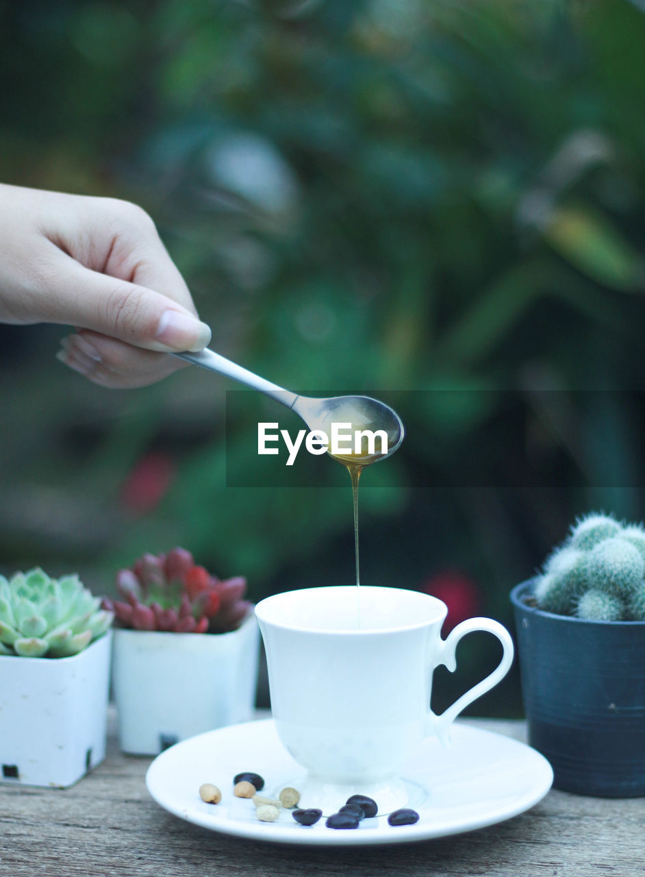 CROPPED IMAGE OF PERSON HOLDING COFFEE CUP ON TABLE AGAINST BLURRED BACKGROUND