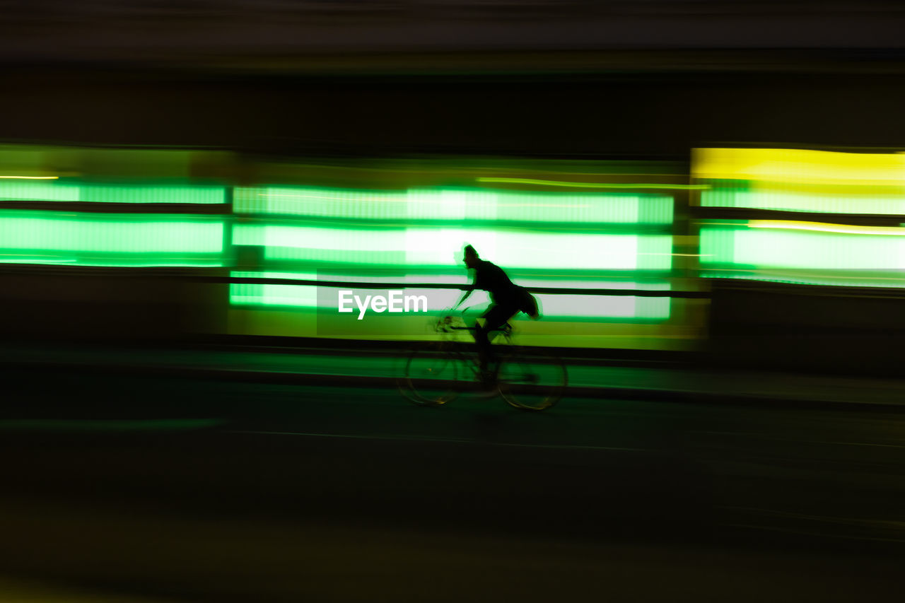 Blurred motion of man riding bicycle on street at night