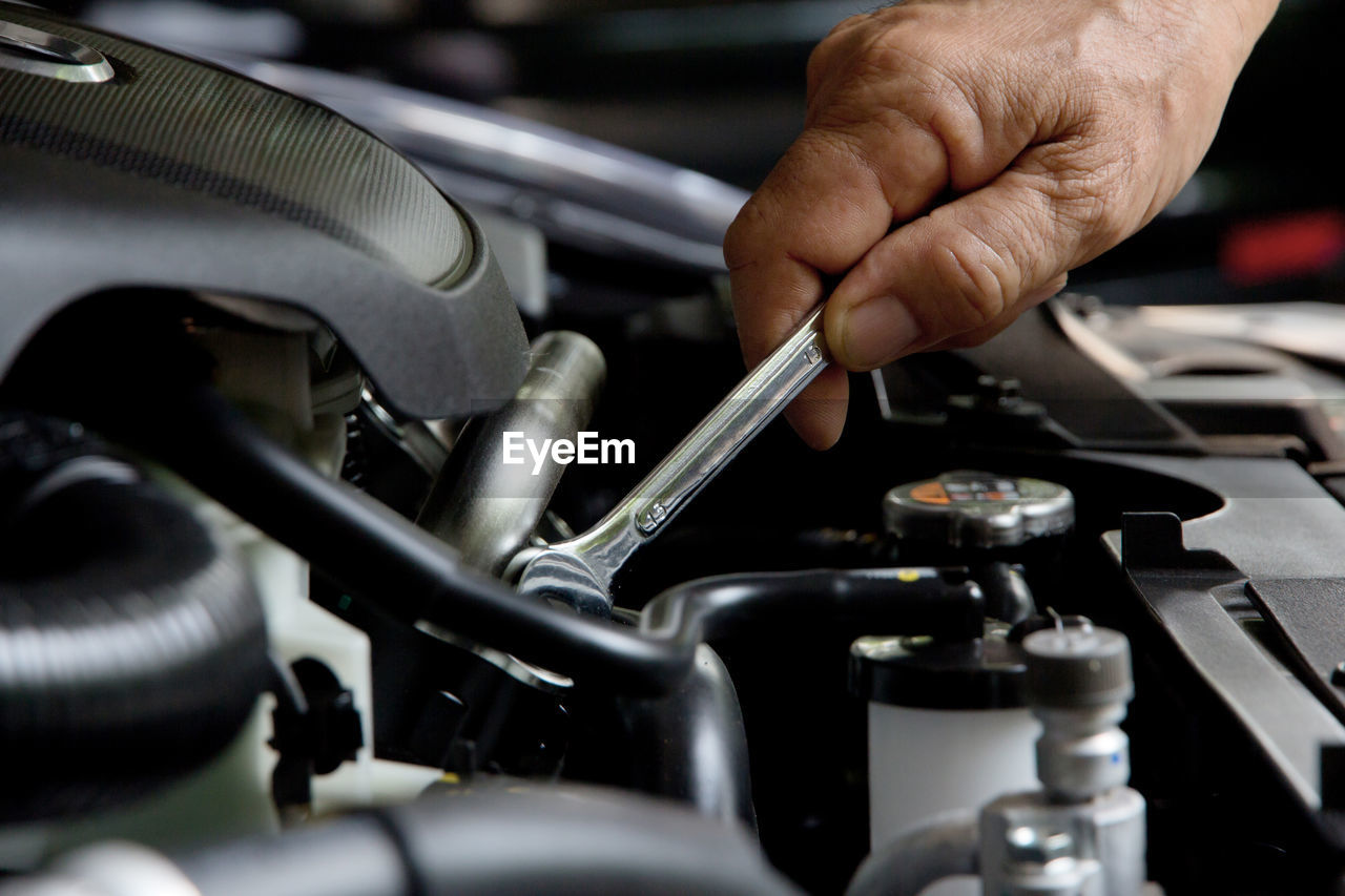 Cropped hand of mechanic repairing car engine with wrench