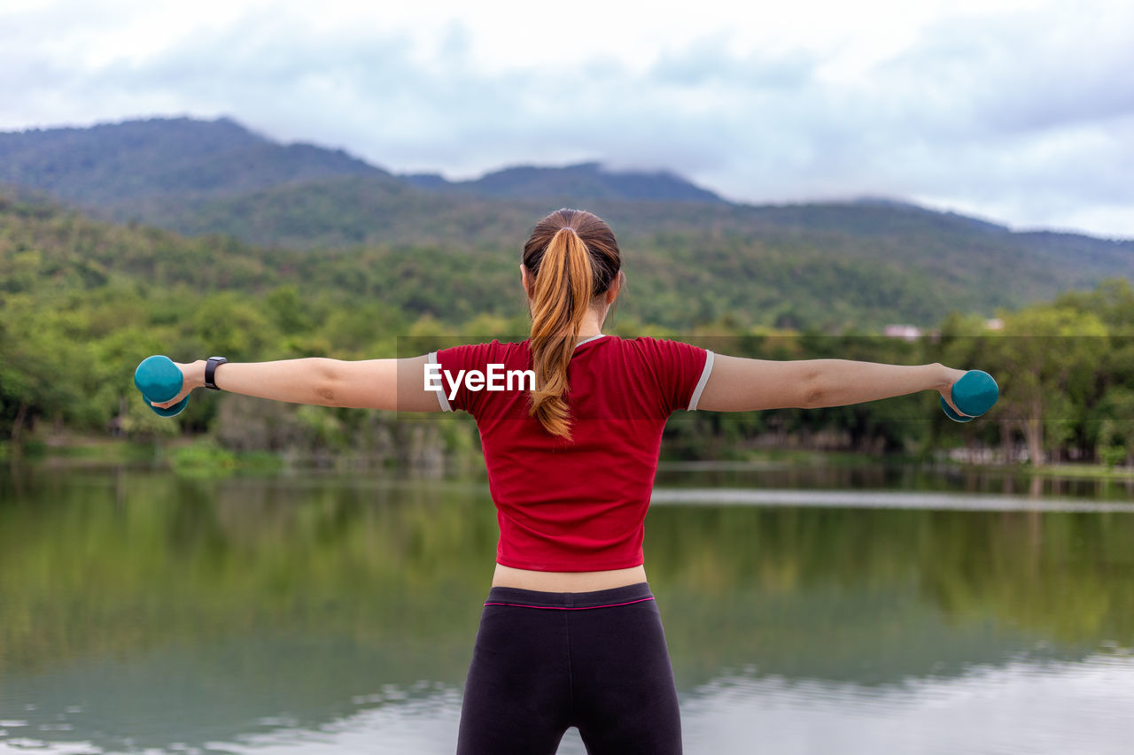 REAR VIEW OF WOMAN STANDING AGAINST CALM LAKE