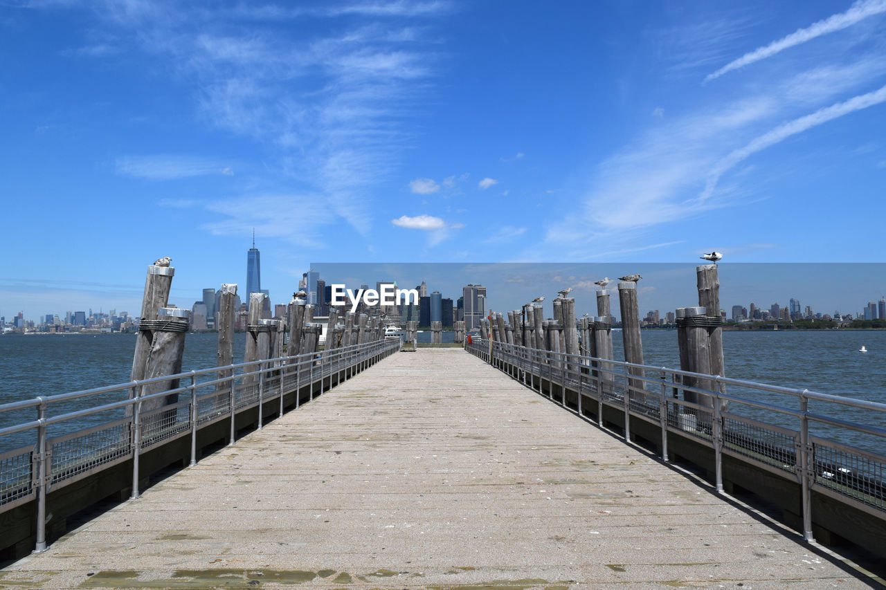 Seagulls perching on wooden columns by empty pier at hudson river against sky