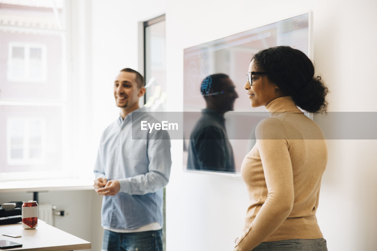 Smiling computer programmers standing by television set during presentation in office