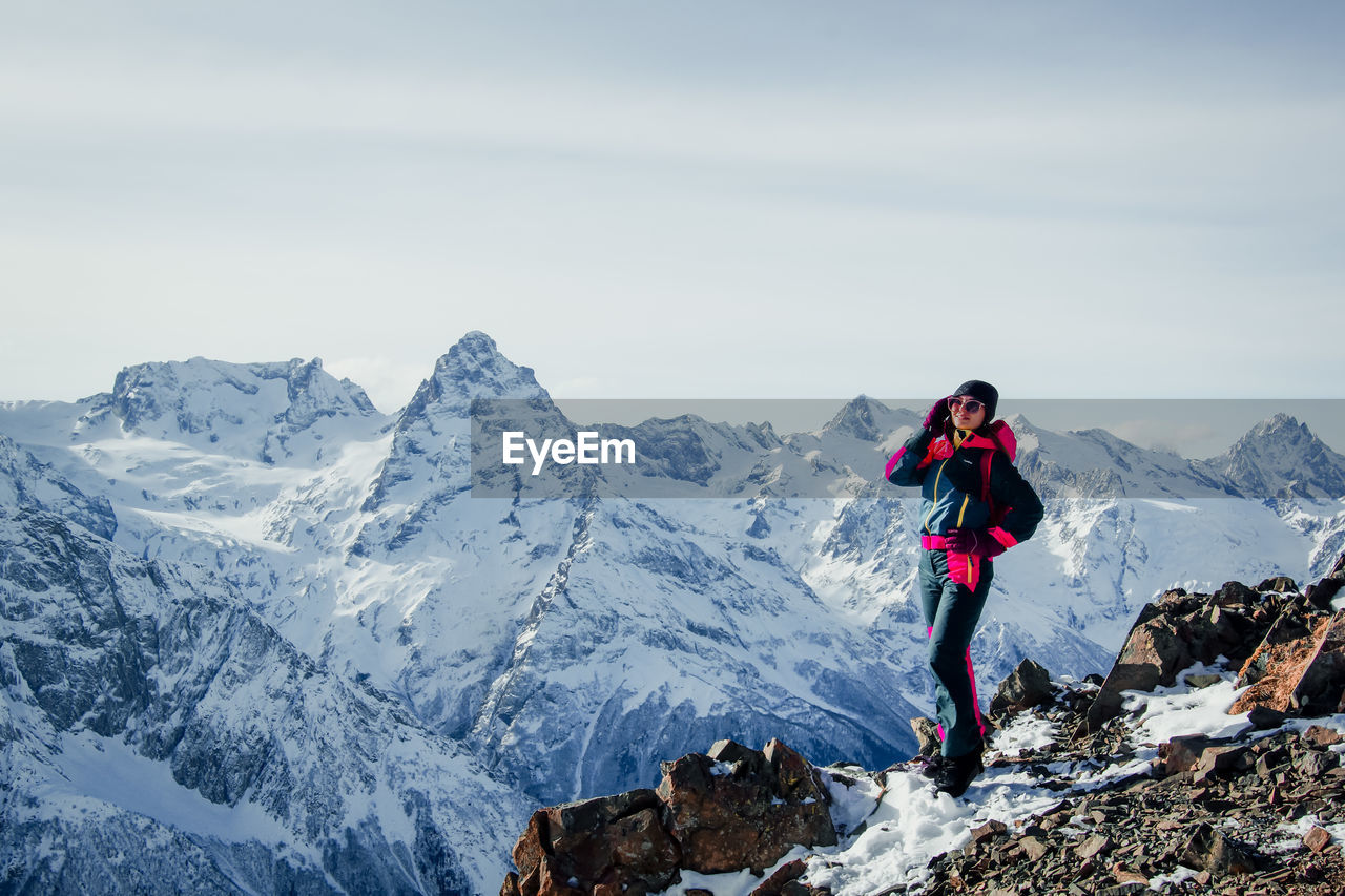 Woman standing on snowcapped mountain against sky