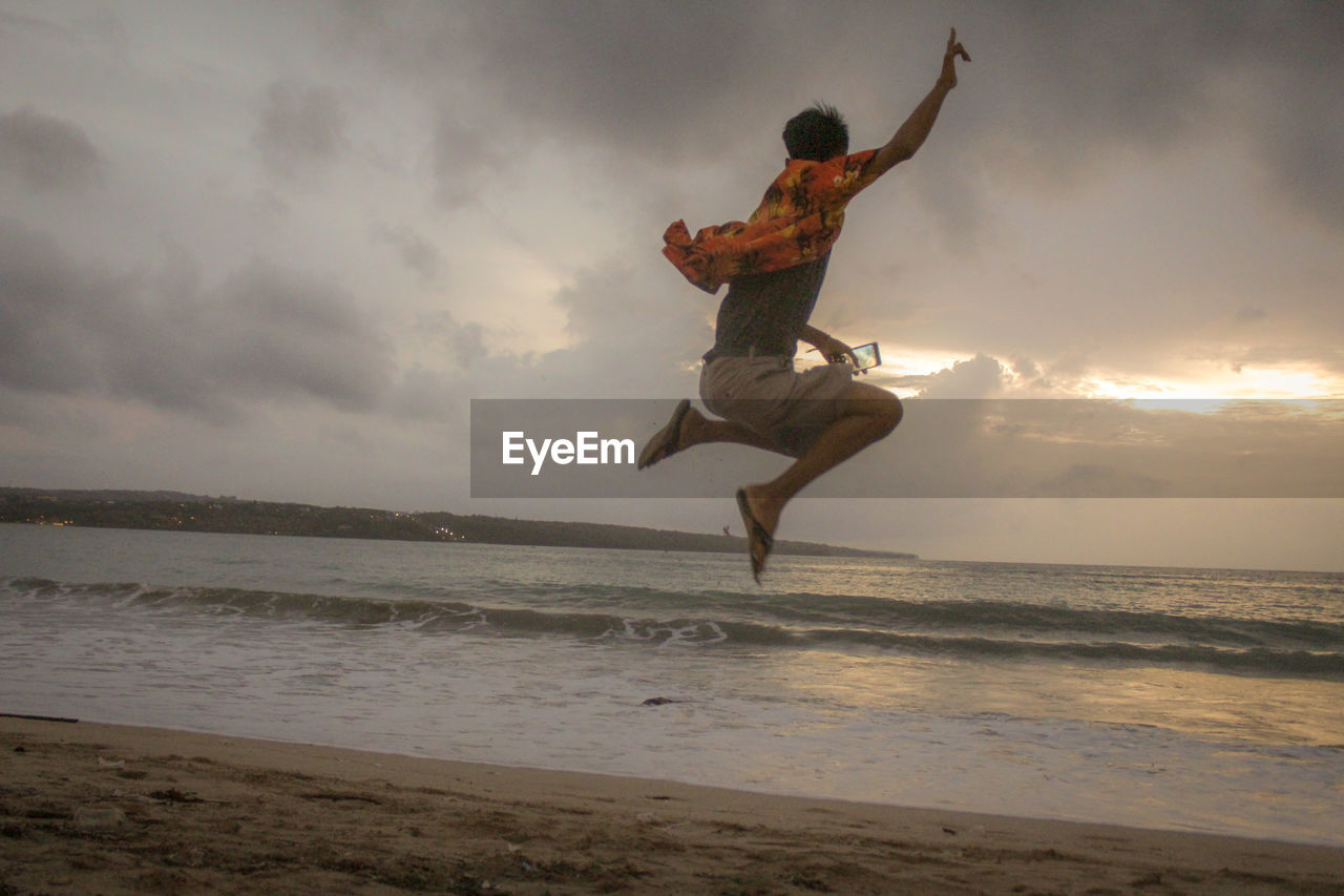 WOMAN JUMPING ON BEACH AGAINST SKY