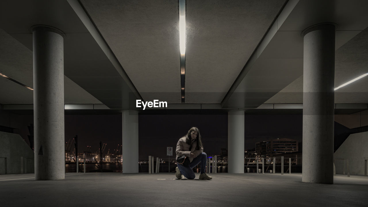 Portrait of girl kneeling in illuminated parking lot at night