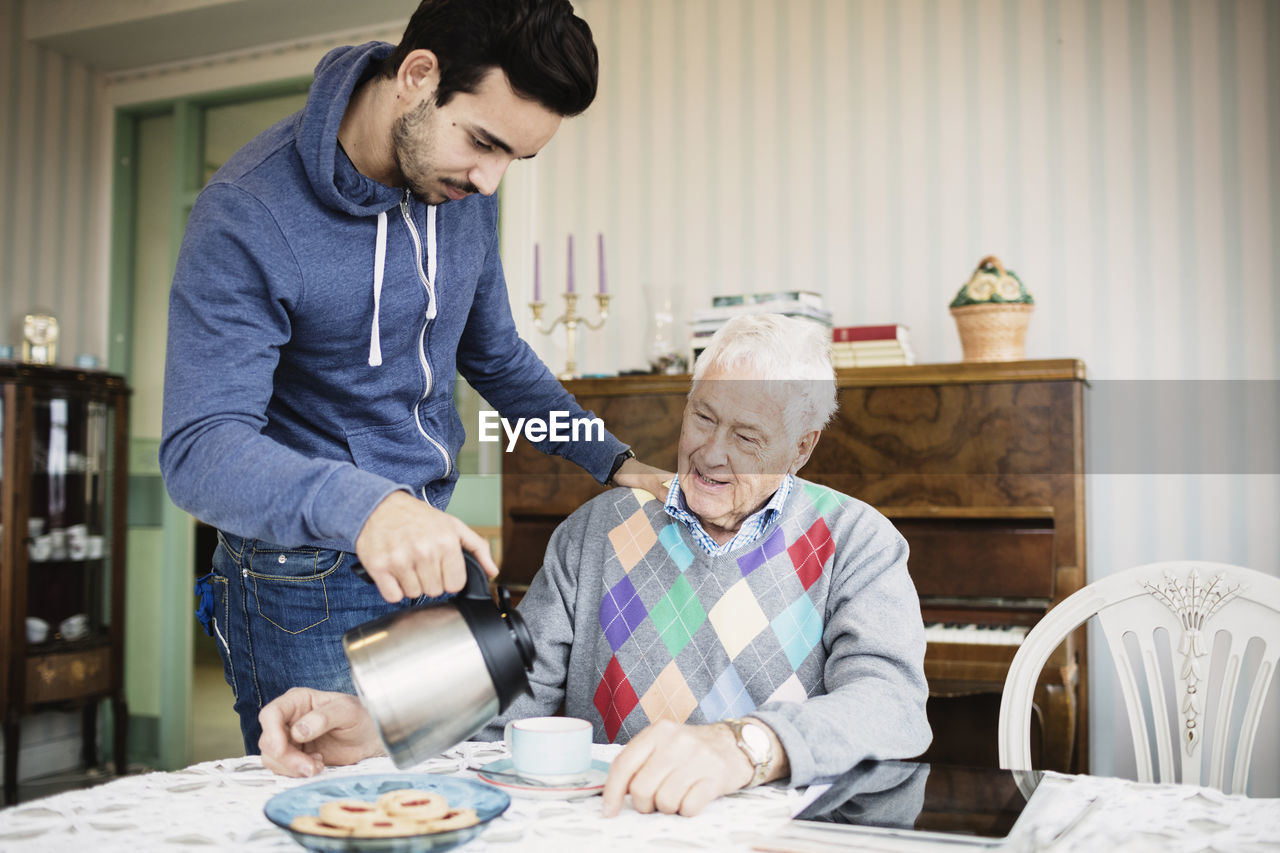 Caretaker serving coffee to senior man at nursing home