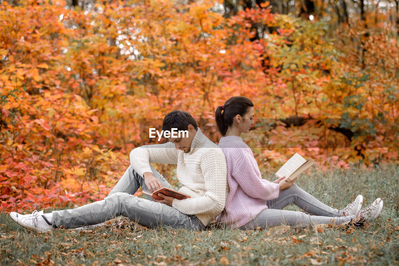 Couple reading books sitting back to back at park
