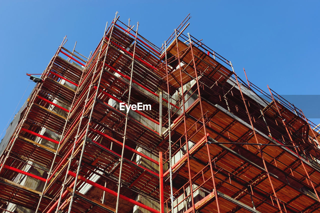 architecture, scaffolding, sky, built structure, industry, building exterior, construction industry, construction site, low angle view, construction, facade, clear sky, tower block, building, nature, incomplete, development, landmark, no people, blue, urban area, skyscraper, city, tower, outdoors, red, day, occupation, construction frame, sunny