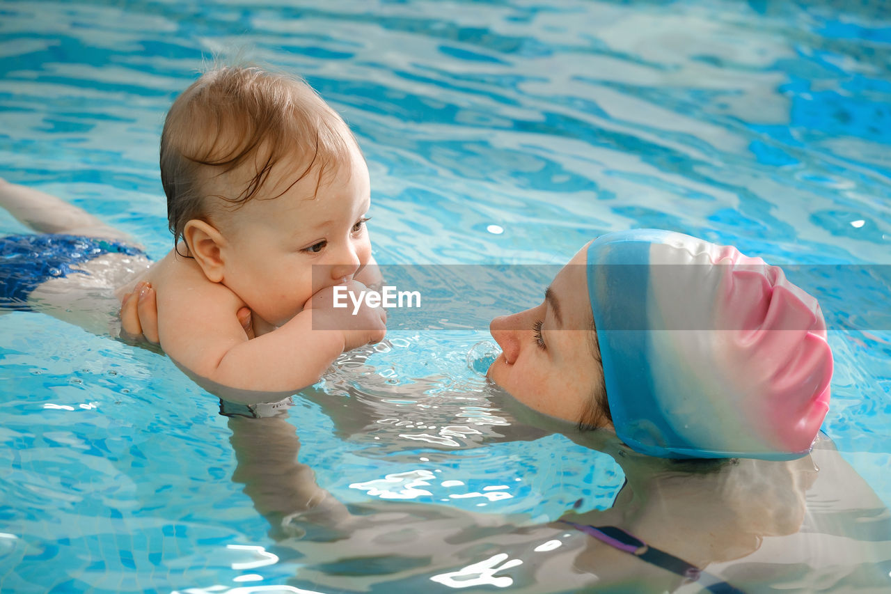 Early age swimming in pool. baby boy trained to swim in water. happy child with trainer woman in