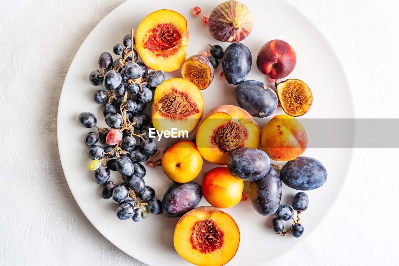 Fresh peaches, plums, blue grapes on white plate, top down view 