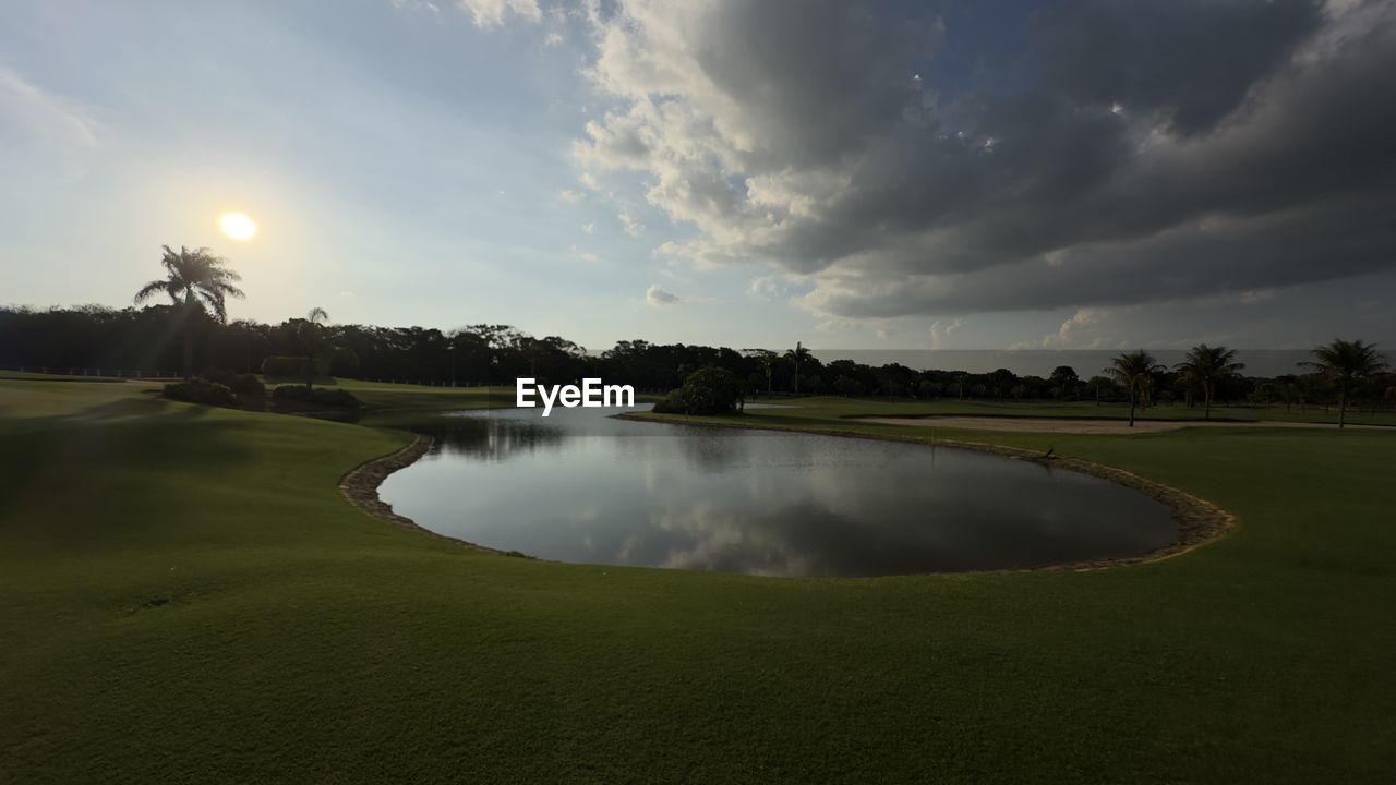sky, golf, activity, golf course, sports, water, grass, plant, sport venue, nature, cloud, environment, leisure activity, tree, scenics - nature, landscape, lake, beauty in nature, green, green - golf course, no people, tranquility, golf club, reflection, land, sunset, outdoors, tranquil scene