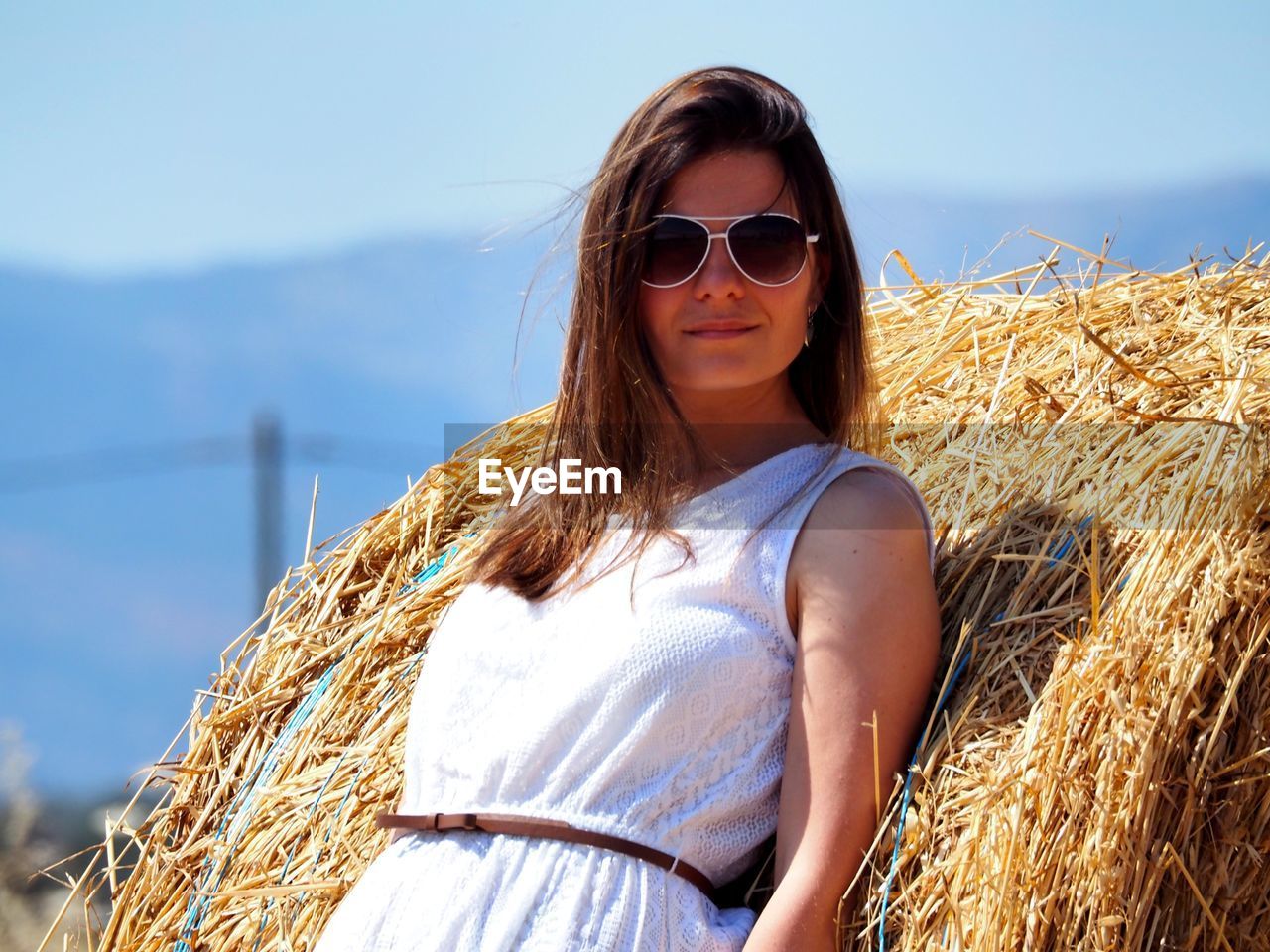Young woman in sunglasses standing by dry grass against clear sky