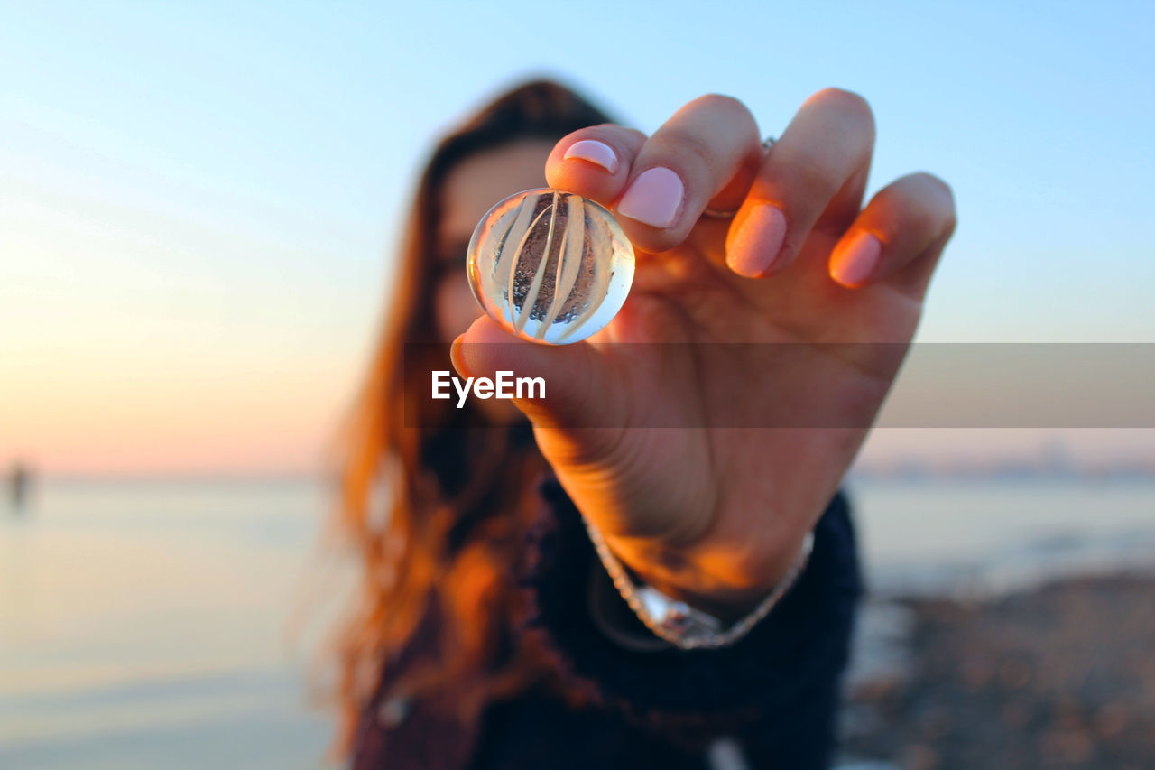 Woman holding marble at beach during sunset