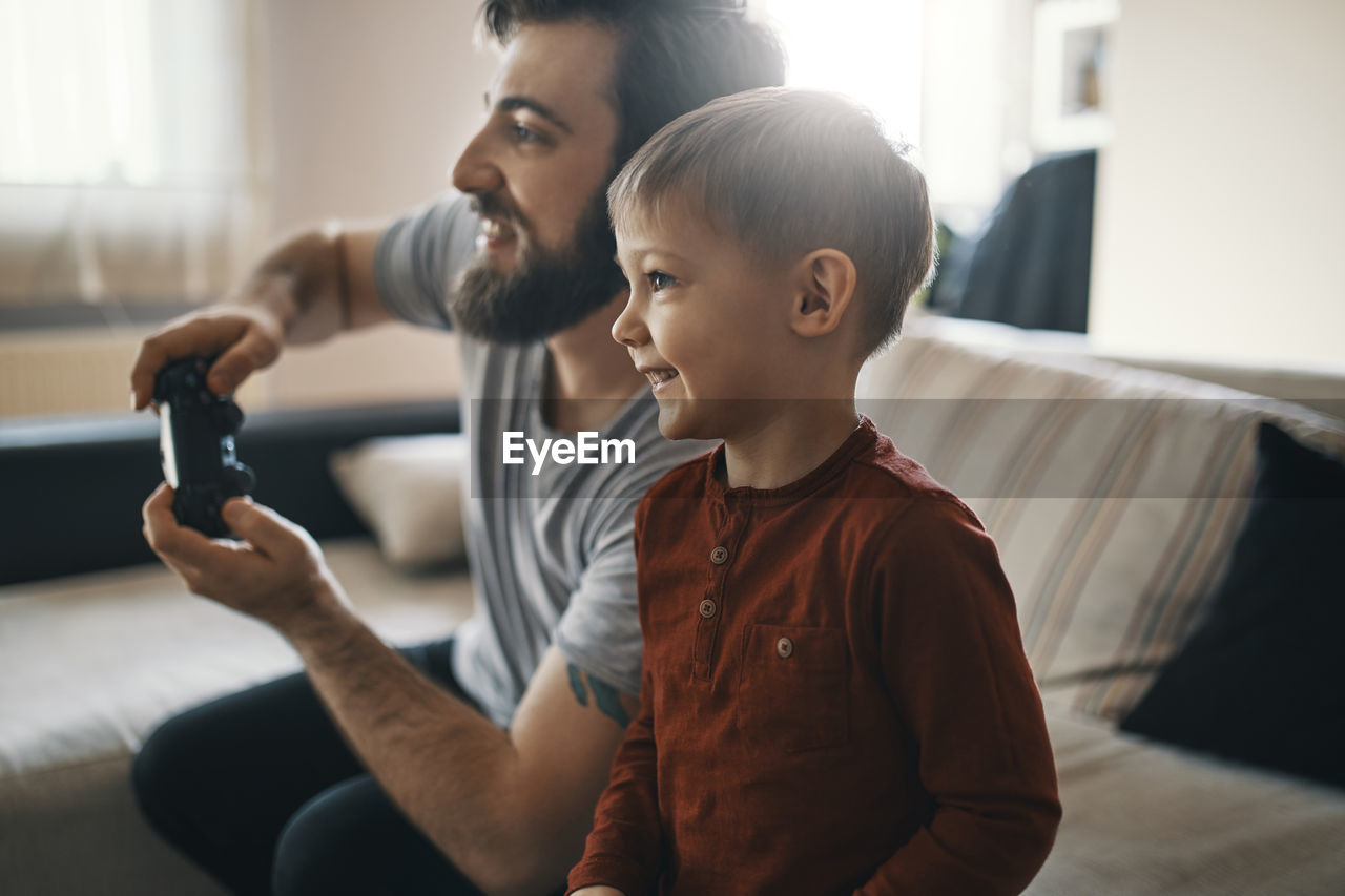 Happy little boy playing computer game with his father at home