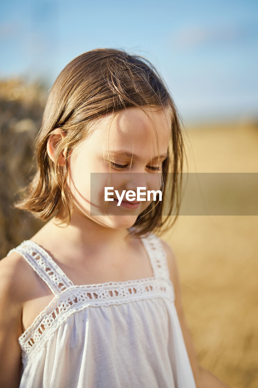 Cute little girl sits on mown rye in the field in summer