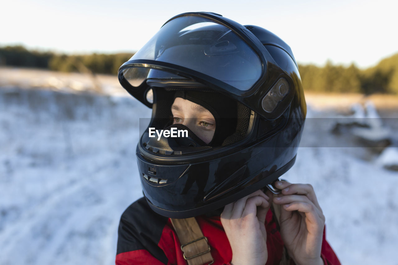 Close-up of teenage boy wearing helmet on snow covered field against sky