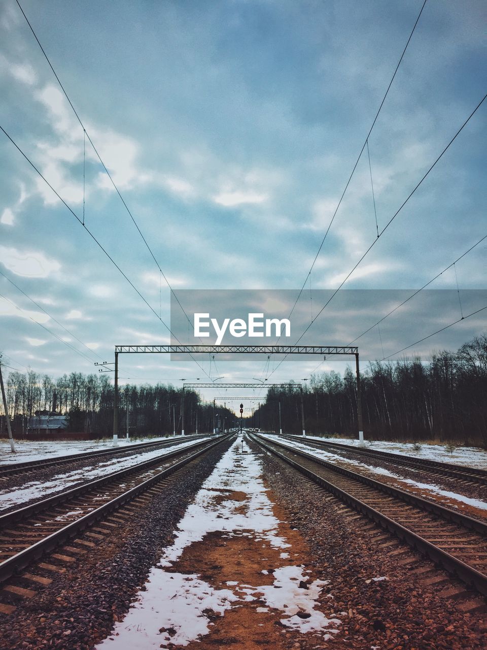 Snow covered railroad tracks against cloudy sky at dusk