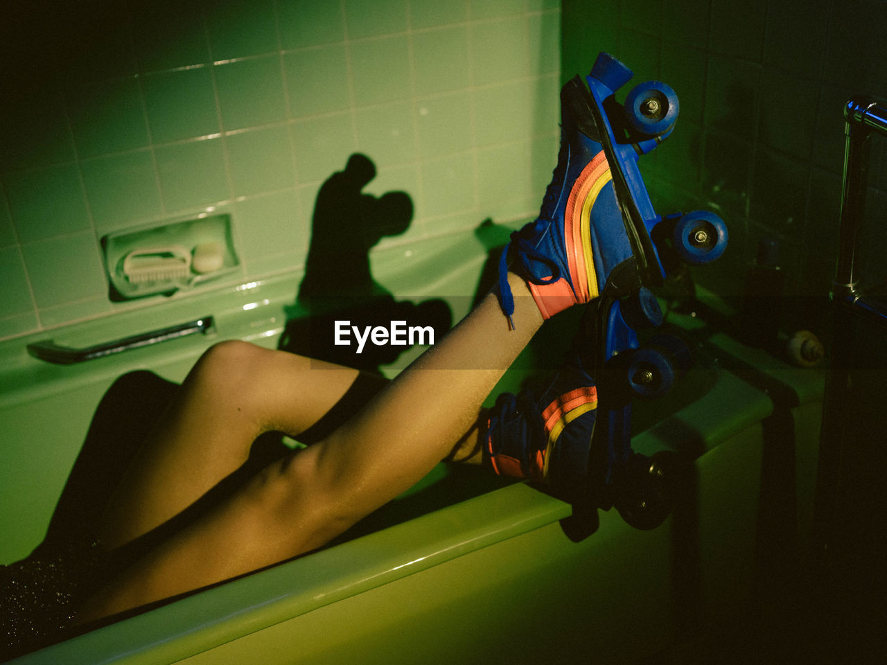 Low section of woman wearing roller skates sitting in bathtub