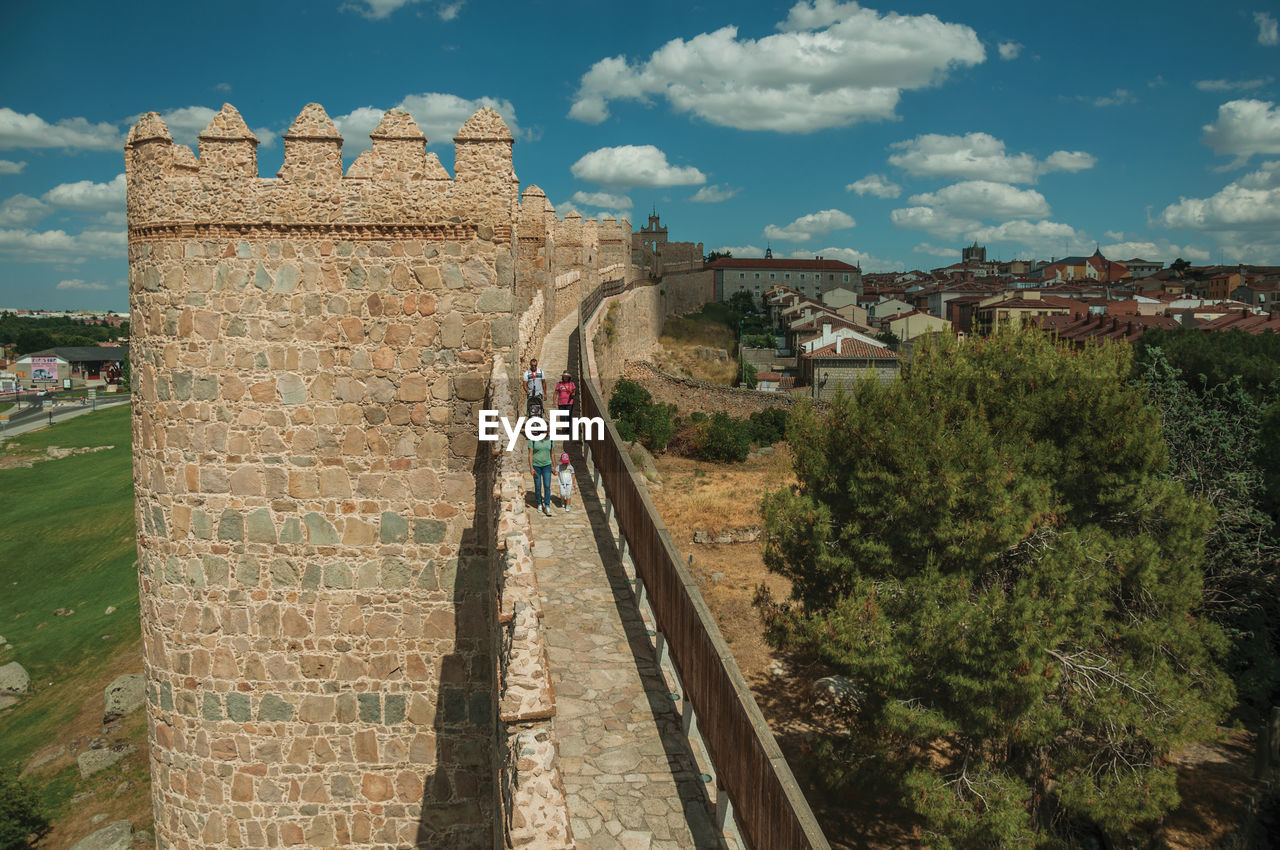 Avila, spain. people on pathway over stone thick wall with large towers encircling avila