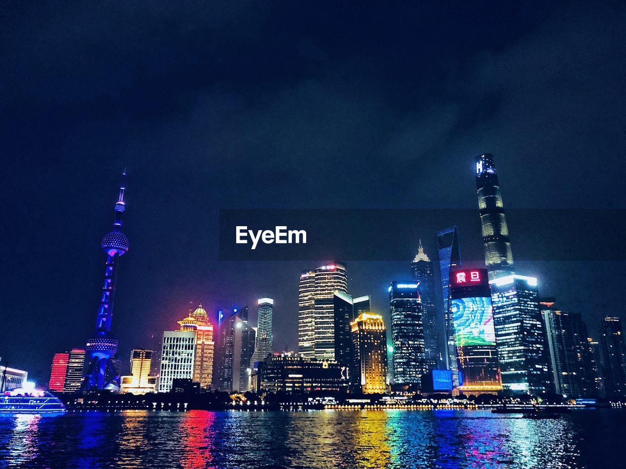 Illuminated buildings by river against sky in city at night